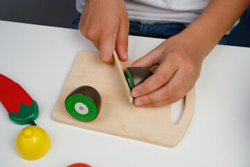 The child plays with wooden colorful toys. The child is cutting a wooden kiwi. Educational logic toys for kid's. Children's hands close-up. Montessori Games for Child Development