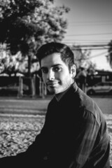 Obraz premium Handsome, young and happy caucasian guy smiling in a park in the afternoon with the sunset light in the face (in black and white)