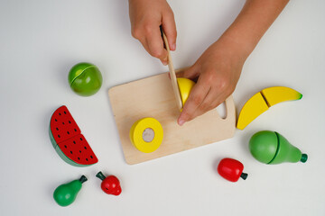 The child plays with wooden colorful toys. The child is cutting a wooden lemon for fruit salad....