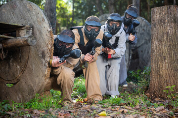 Group of people in camouflages and masks playing paintball aiming with gun in shootout outdoors