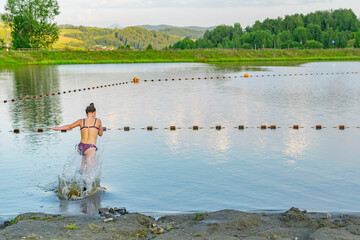 a teenage girl runs to dive into the water on a pond with fencing buoys on an artificial lake