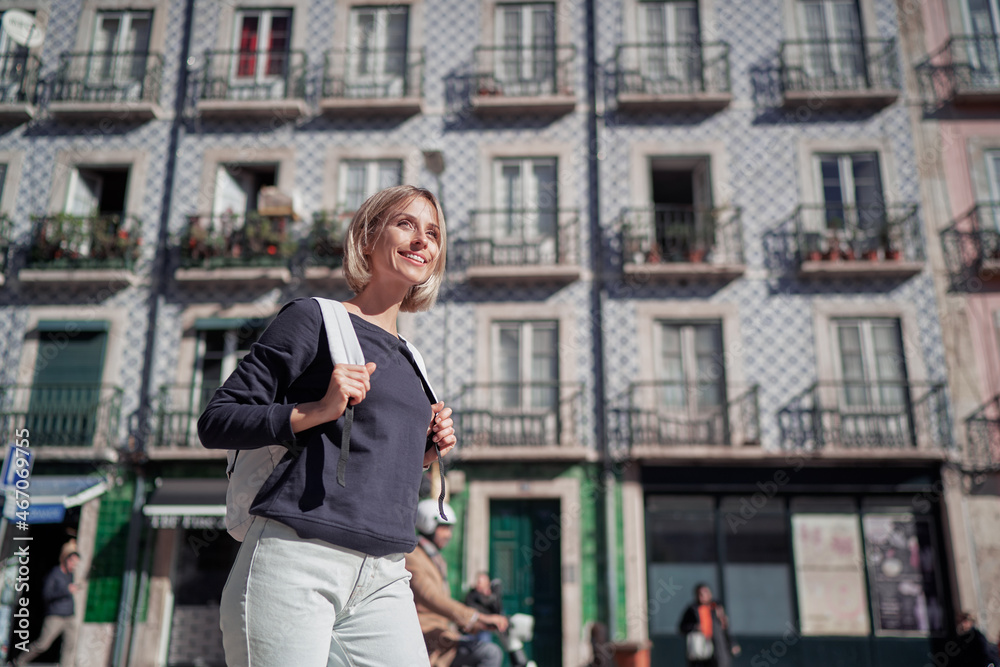 Wall mural Traveling by Portugal. Happy young woman with rucksack walking by streets in Lisbon.