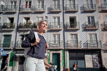 Traveling by Portugal. Happy young woman with rucksack walking by streets in Lisbon.