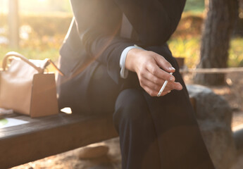 Fototapeta premium A woman is sitting on a park bench and smoking a cigarette