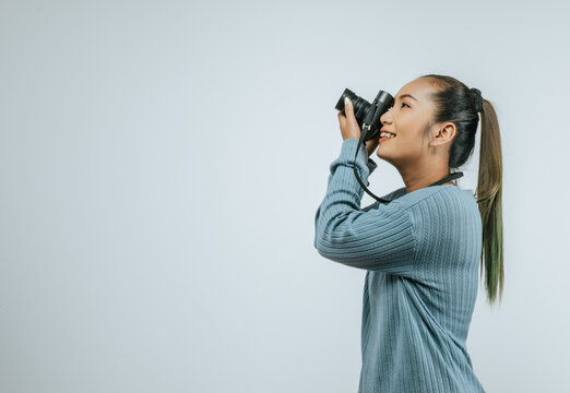 Portrait of Asian woman wearing casual clothes with a big smile on face looking to side,  taking pictures with camera. Isolated background in studio with blank space.
