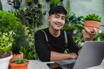 Young gardener man use smartphone and laptop online with houseplant