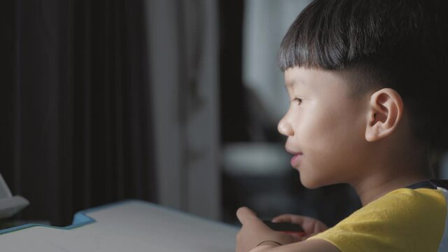 Asian boy about 5 years old using a wireless controller for playing a video game.