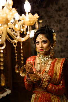 Portrait of very beautiful young Indian bride in luxurious bridal costume with makeup and heavy jewellery looking at Chandelier. Classic vintage interior. Lifestyle Wedding fashion.