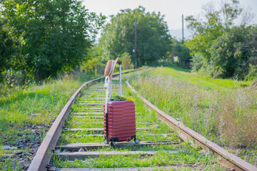 a red suitcase and a hat on the railroad stands