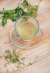 Cancer bush tea, traditional herbal medicine made from Sutherlandia plant. tea in glass cup on a wooden surface with scattered loose leaf tea and fresh Cancerbush leaved with copy space