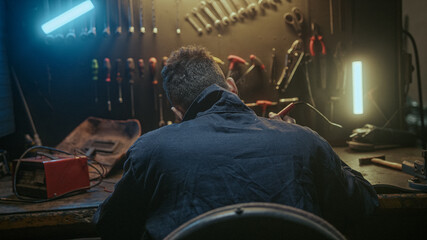 Back shot of male workshop worker sitting and solder on workbench