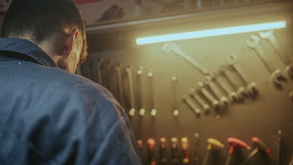 Young blacksmith male person picking up his tools from the bench to do work