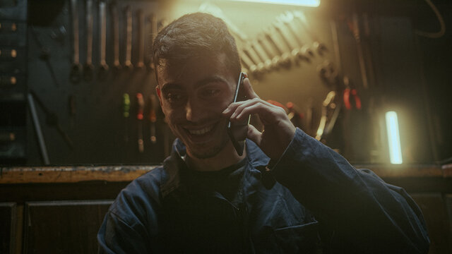 Handsome determined blacksmith man sitting in front of the workbench and he using smartphone call friends or her family