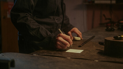 Worker man taking measurements from an iron stick and taking note on paper. Man in work in small iron workshop