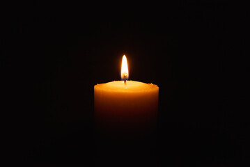 One single light candle burning brightly in the black background.Spiritual candle yellow flame. Flame of candle in the darkness.Copy space.