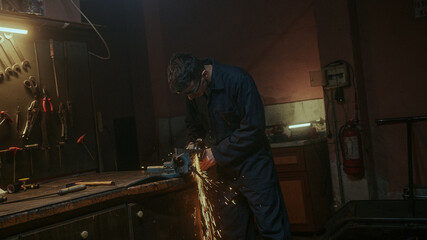 Young blacksmith man use iron or metal cutting machine and he metal grinding on steel spare part in...