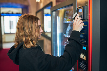 Woman paying for product at vending machine using smartphone