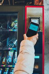 Woman paying for product at vending machine using smartphone - obrazy, fototapety, plakaty