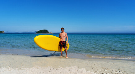 Active male surfer running with surfboard on sand beach enjoying healthy lifestyle extreme sport