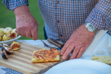 Elderly man spread fig jam on slices of bread outdoor.