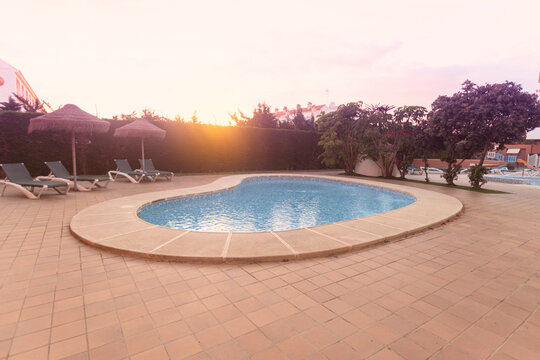 Photography of deck chair and umbrella and a pool, a residential area during the sunset with palms and pool