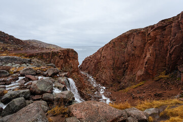 Fototapeta na wymiar Rocks, a waterfall and the Barents Sea near the village of Teriberka