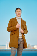 Young man in checkered trousers, sweater wraps wool coat outdoor
