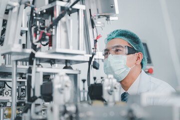Naklejka premium Both male and female Asian scientists are outfitted with protective gear. Examining the factory's machinery and materials used in the mask-making process. Covid 19 is a piece of preventive equipment.