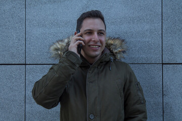 young man in coat and mobile phone with wall background