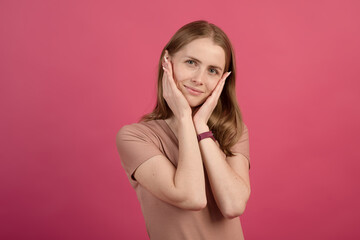 Fototapeta premium Portrait of a young and attractive Caucasian blonde girl on a pink studio background.