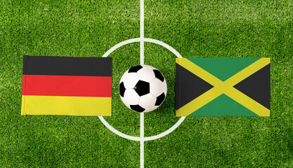 Top view soccer ball with Germany vs. Jamaica flags match on green football field.