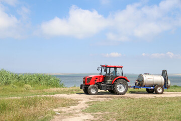 A farmer drives a tractor with a sprayer attached along the bay and reeds. Agriculture