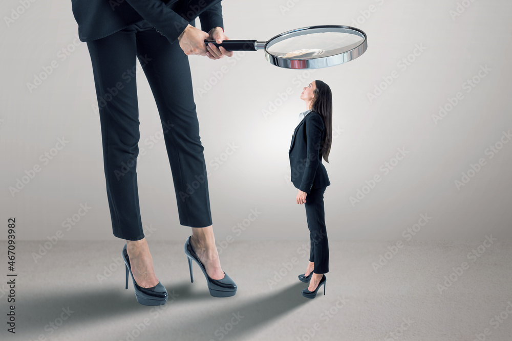 Poster Businessperson in suit using magnifier magnifying glass to look at tiny female subordinate on concrete background with shadow and mock up place. Hiring and dominance concept.