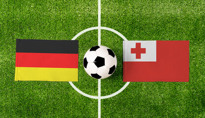 Top view soccer ball with Germany vs. Tonga flags match on green football field.