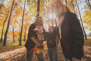 Grandmother and mother with granddaughter having fun with dog in autumn season. Generation, leisure and family concept