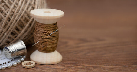 Fototapeta na wymiar A spool of brown thread, a needle and a thimble on a wooden background.Accessories for sewing and needlework
