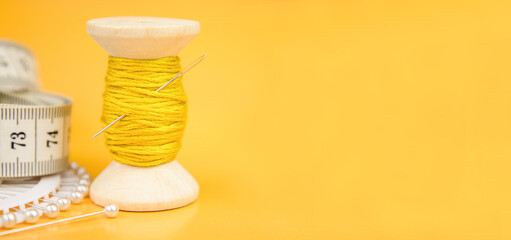A spool of yellow thread, a needle and a thimble on a yellow background.Accessories for sewing and...