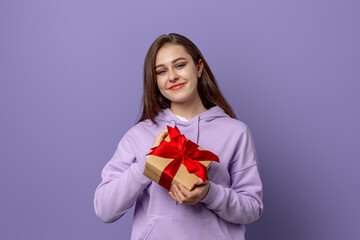 Happy young brunette woman dressed casual hoodie, standing isolated over purple background, holding...