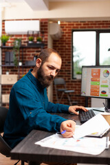 Fototapeta premium Businessman sitting at desk analyzing business paperwork working at management presentation planning company strategy in startup office. Entrepreneur looking at marketing documents