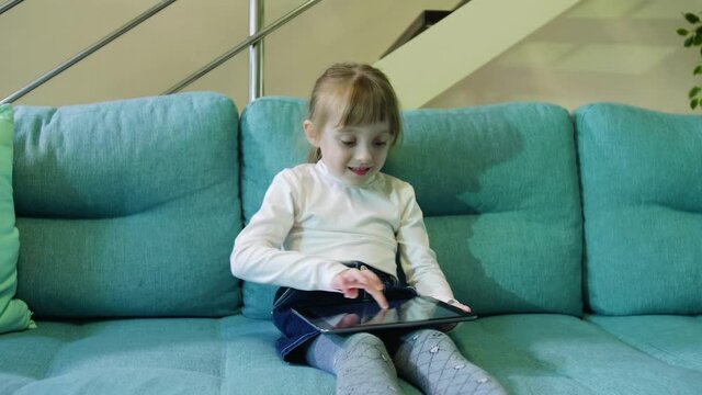 Adorable Kid Girl Using Digital Tablet Watching Cartoons at Home. Close up Portrait of Cute Child Playing Game on Tablet PC Relaxing on Sofa