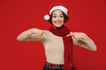 Young impressed exultant surprised woman 20s wear Santa Claus Christmas red hat point index finger on herself isolated on plain red background studio portrait. Happy New Year 2022 celebration concept.