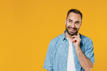 Young smiling happy pensive minded thoughtful caucasian man 20s in blue shirt white t-shirt look aside on copy space workspace area prop up chin isolated on plain yellow background studio portrait