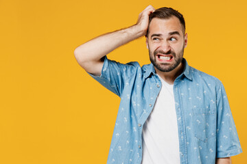 Young puzzled embarrassed bewildered caucasian man 20s wearing blue shirt white t-shirt scratch head look aside say oops isolated on plain yellow background studio portrait. People lifestyle concept. - obrazy, fototapety, plakaty