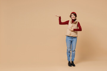 Full body young woman 20s wears red turtleneck vest beret point finger on scale, show and measure height, compare isolated on plain pastel beige background studio portrait. People lifestyle concept.