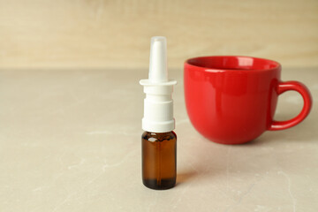Blank bottle of nasal spray and cup of tea on light table