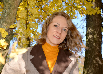 Portrait of a woman in a coat against a background of yellow autumn foliage