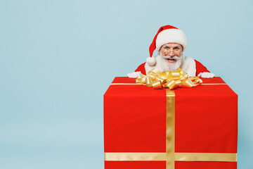 Full size old Santa Claus man 50s in Christmas hat red suit clothes stand near big gift box isolated on plain blue background studio. Happy New Year 2022 celebration merry ho x-mas holiday concept