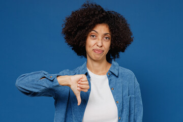 Young displeased upset unhappy black woman in casual clothes shirt white t-shirt showing thumb down dislike gesture isolated on plain dark blue background studio portrait. People lifestyle concept