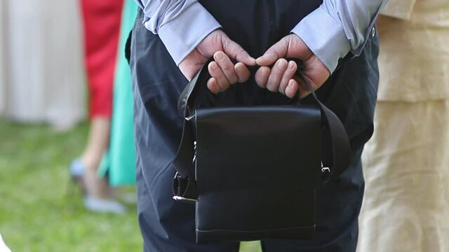 leather black bag close-up in the hands of a man behind his back. men's messenger bag. accessory