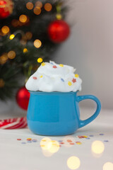 blue cup with drink decorated with whipped cream on table near festive christmas tree